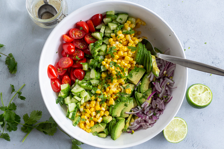 Corn tomato Avocado salad in a bowl with dressing next to it