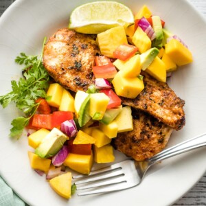 White plate with a serving of jerk chicken and mango avocado salsa.