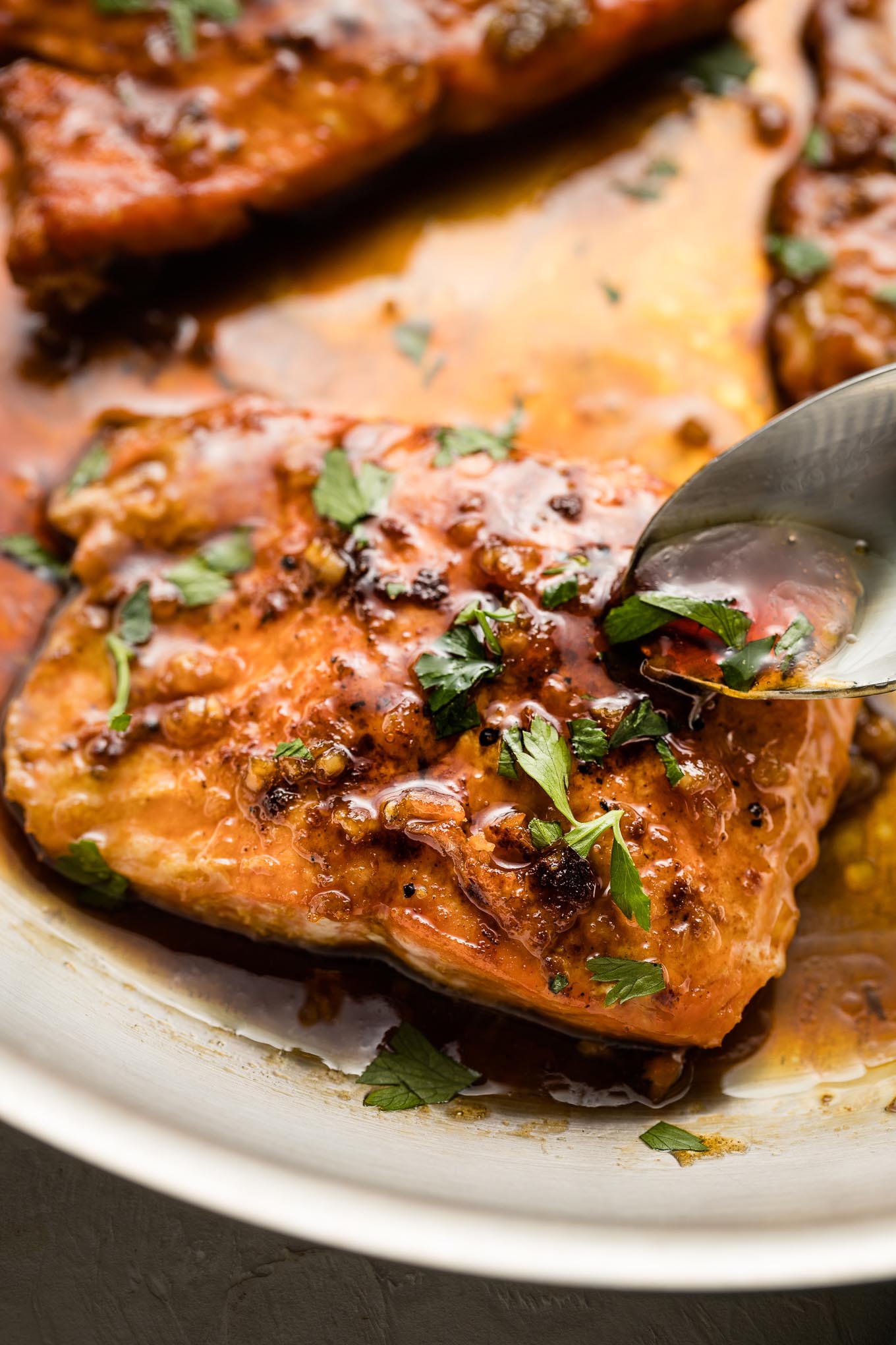 Spoon pouring sauce over cooked salmon filets.