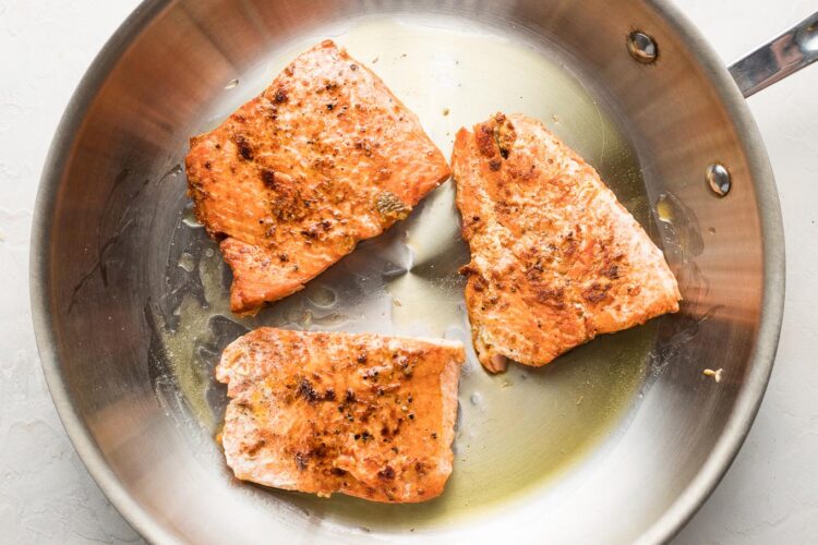 Pan-seared salmon filets in a skillet.