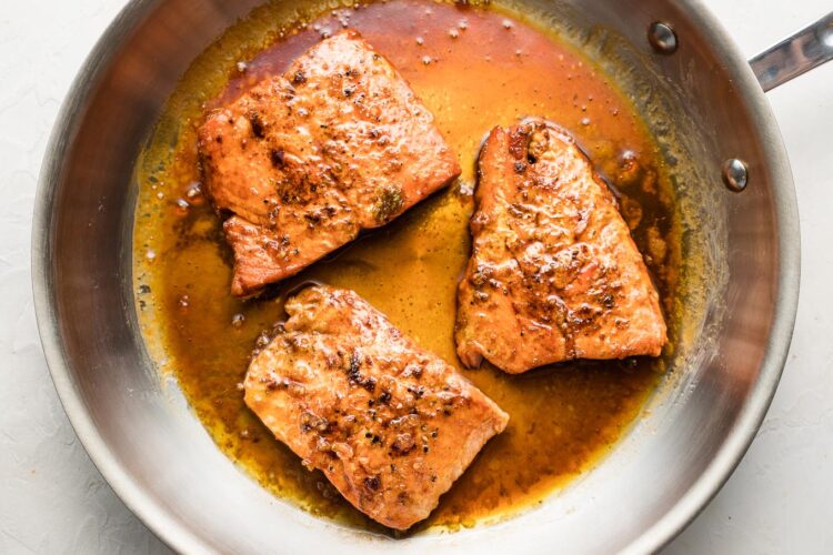 Seared salmon filets with sauce in skillet.