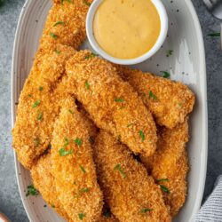 Crispy chicken tenders on a plate with honey mustard.
