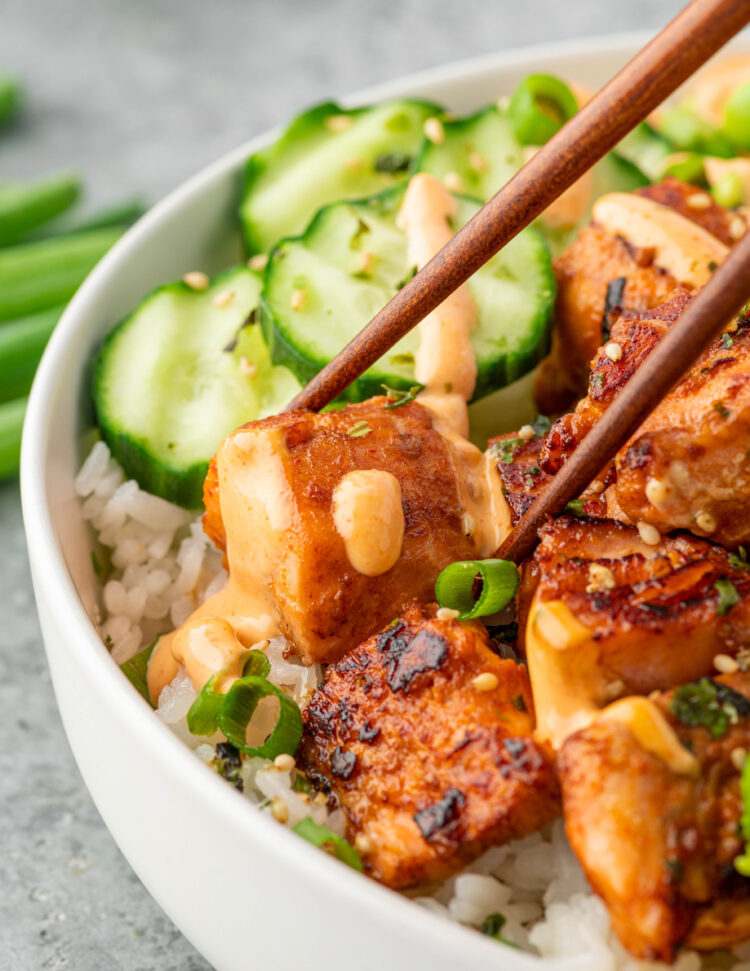 Using chopsticks to hold a piece of spicy salmon with sauce.