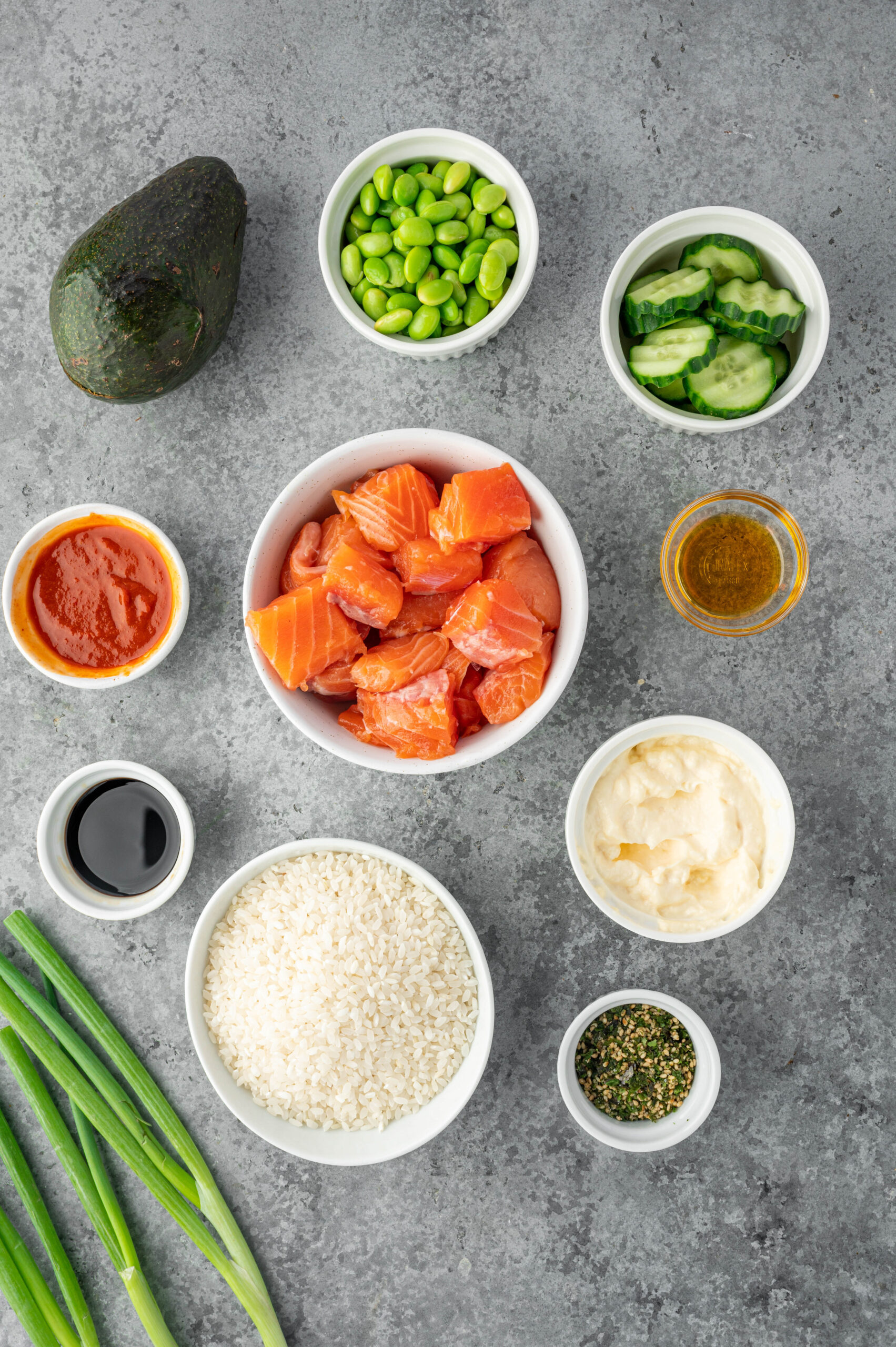 Raw salmon pieces, cucumber slices, green onion, sauces and an avocado.