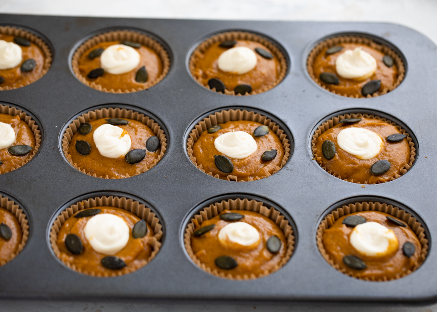 Adding pumpkin muffin batter to a pan.