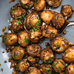 Serving mushrooms out of a pan with a large spoon.
