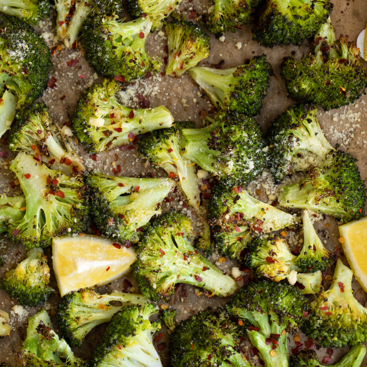 Roasted broccoli on a pan with lemon wedges.