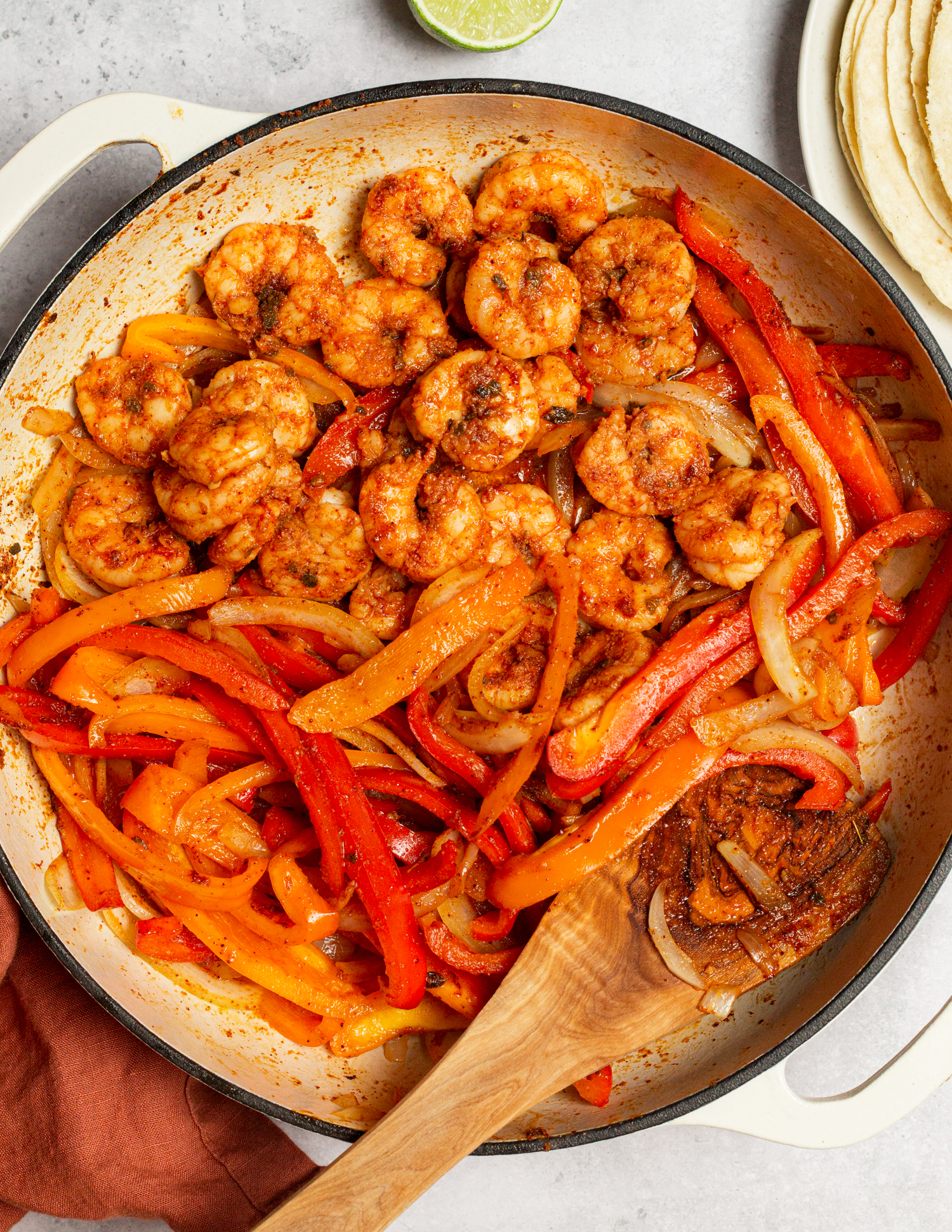 Using a wooden spoon to stir shrimp fajitas in a skillet.