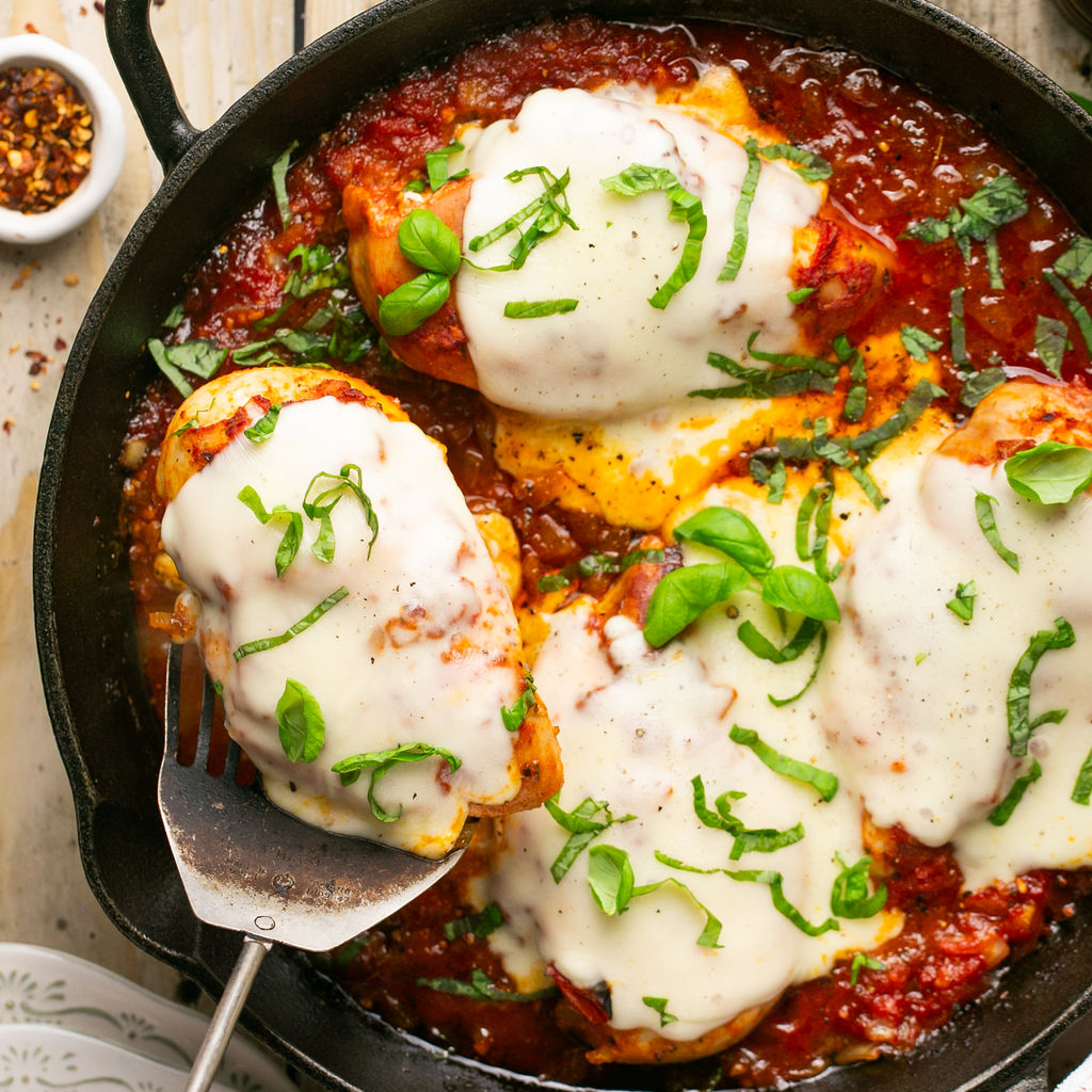 Serving chicken covered in mozzarella from a skillet.